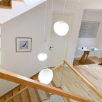 A Clérachic white pebble pendant hangs above an oak handrail in a hallway with a white door and a small desk.