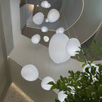 Large and small Clérachic white pebble pendants hang in a stairwell, with a green plant at the edge of the frame.