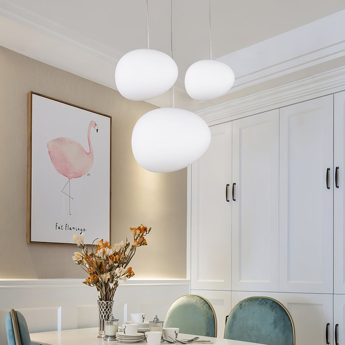 Close view of three Clérachic white glass pebble pendants in a dining room with a flamingo print and teal chairs.