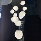 Cluster of Clérachic white pebble pendants against dark walls in a stairwell, lit from the largest at the bottom.