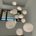 Large Clérachic white pebble pendants fill a double-height room, with a window and a pale wall behind.