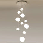 A tight cluster of Clérachic white glass pebble pendants hangs from a round white canopy on a plain ceiling.