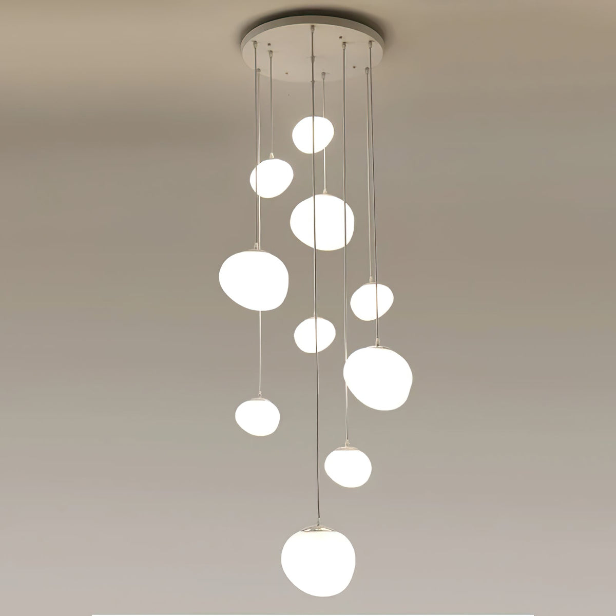 A tight cluster of Clérachic white glass pebble pendants hangs from a round white canopy on a plain ceiling.