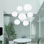 Seven Clérachic white glass pebble pendants hang above a round white table in a glass-walled meeting room.
