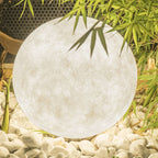 Close view of the veined, fibre-textured surface of a big Clérachic sphere lamp, set on white pebbles under bamboo leaves.