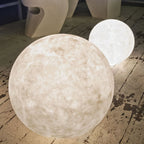 Two textured Clérachic spheres of different sizes on a worn grey wooden floor, the nearer one unlit and the smaller one glowing.