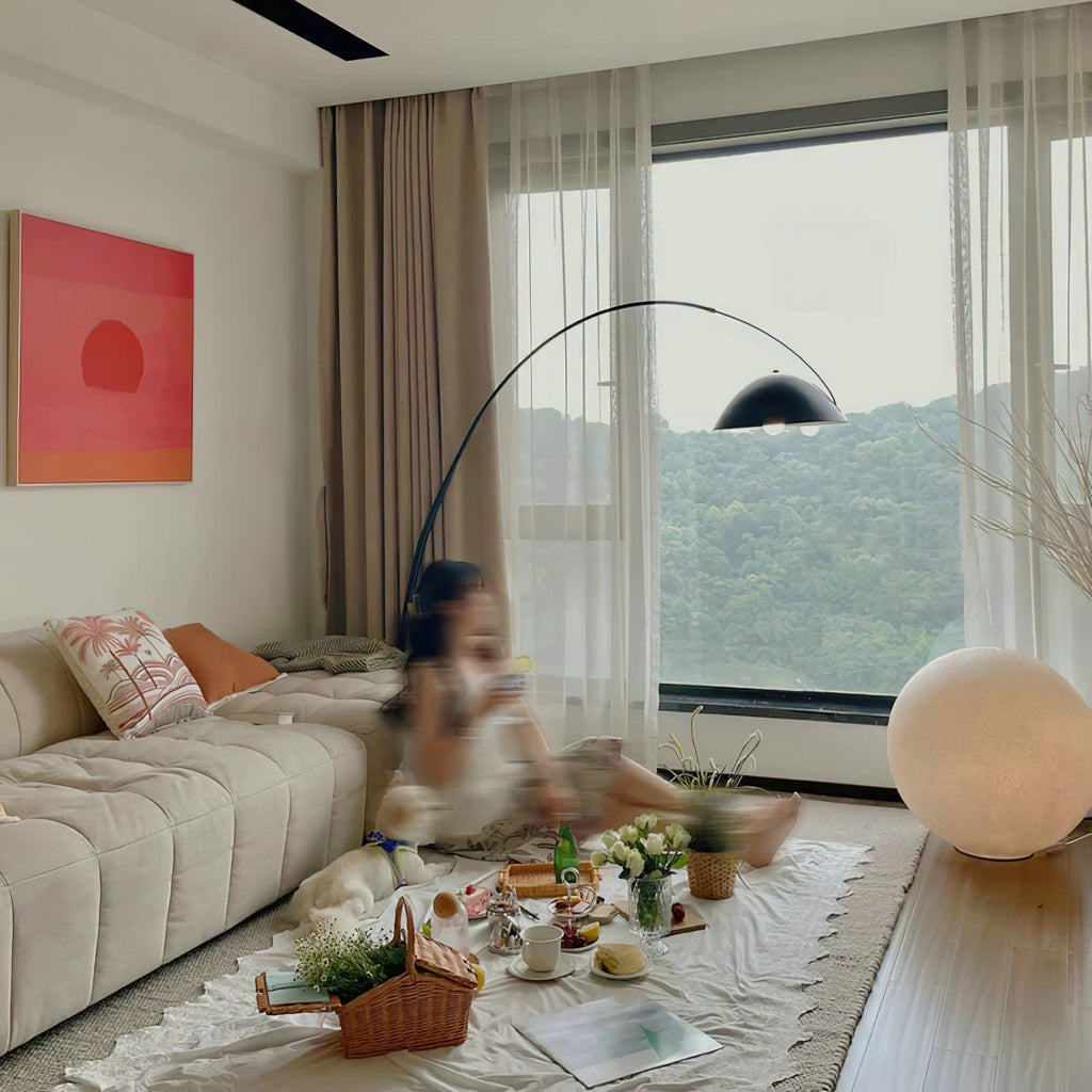 Clérachic sphere lamp on the floor of a bright living room by a large window, with people picnicking on a rug nearby.
