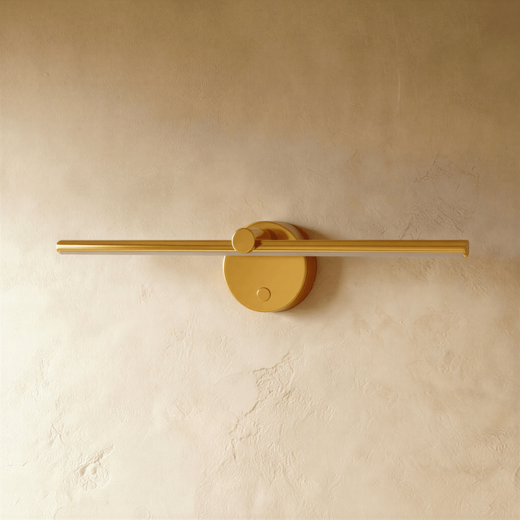 Clérachic wall lamp in brushed gold, the slender bar and round backplate shown unlit against a plaster wall.