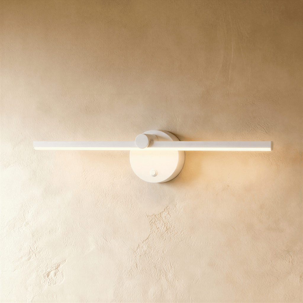 Clérachic wall lamp in white, its slim linear bar casting warm light beside a round switch-knob backplate.