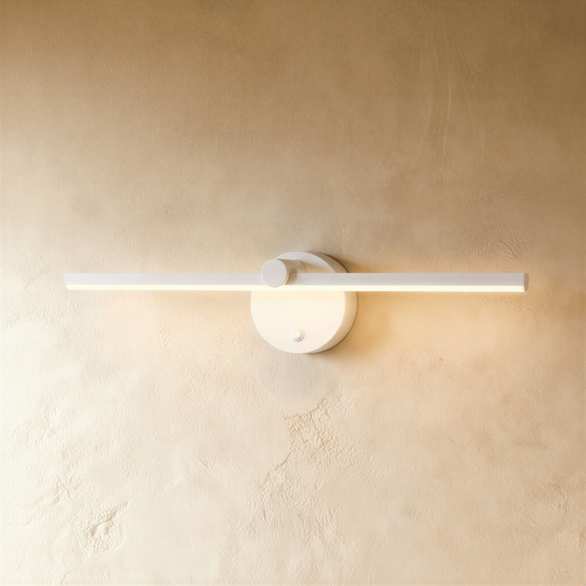 Clérachic wall lamp in white, its slim linear bar casting warm light beside a round switch-knob backplate.