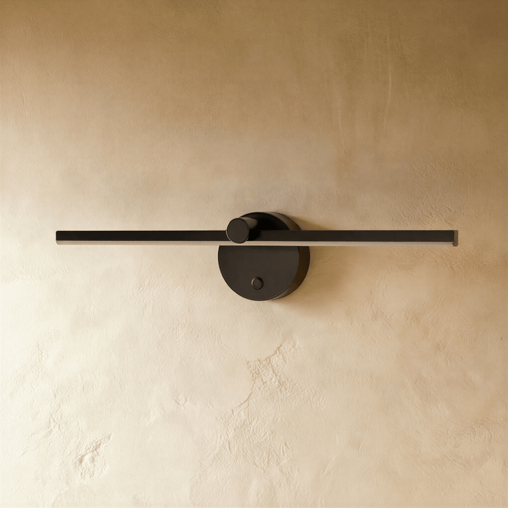 Clérachic wall lamp in matte black, the slender bar and round backplate shown unlit against a plaster wall.