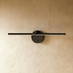 Clérachic wall lamp in matte black, the slender bar and round backplate shown unlit against a plaster wall.