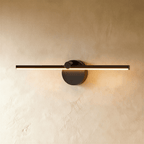 Clérachic wall lamp in matte black, the slim linear bar glowing warm white against a plaster wall.