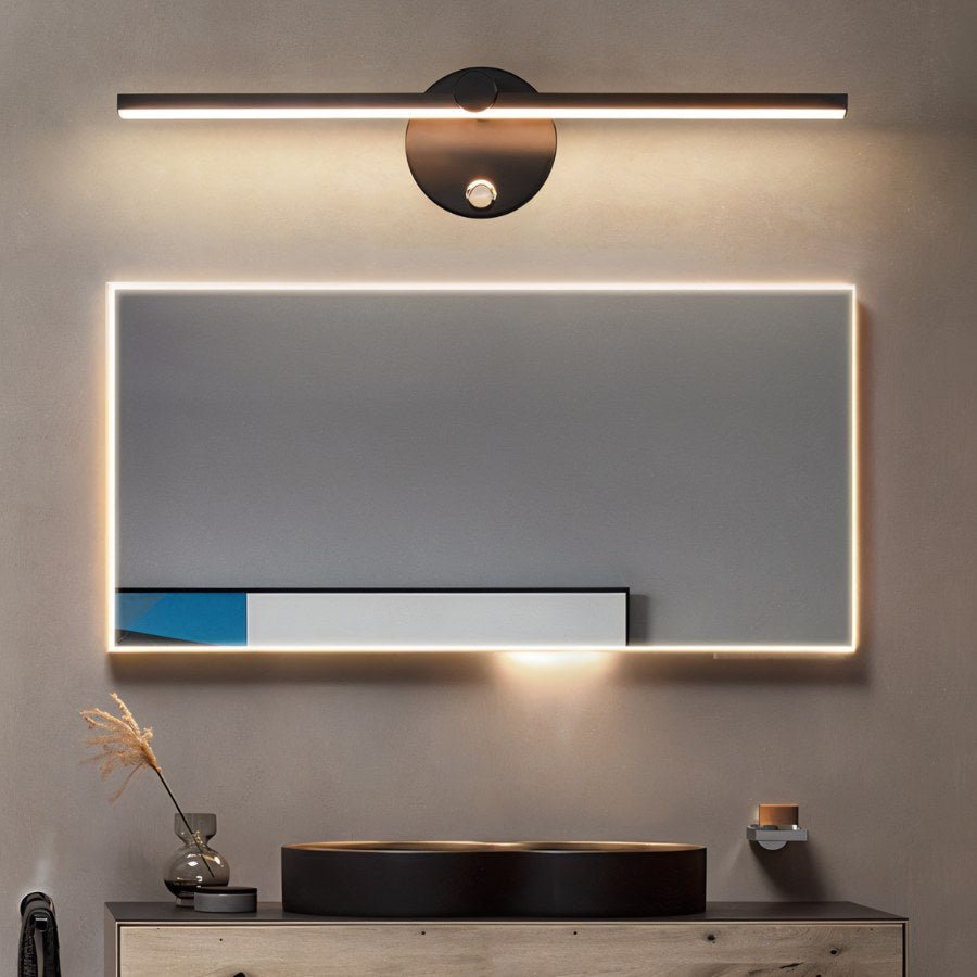 Clérachic wall lamp in black mounted above a backlit mirror, glowing warm white over a round black sink.