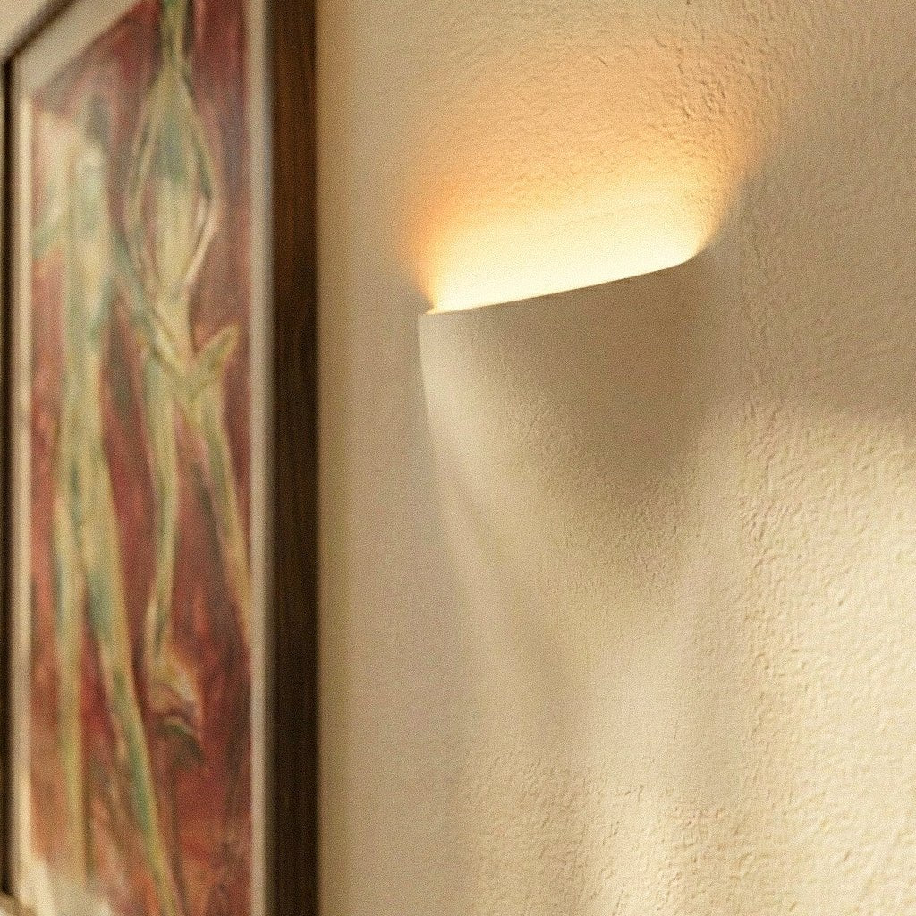Close-up of a Clérachic trimless wall light glowing softly into plaster, beside the edge of a framed painting.