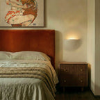 A Clérachic trimless wall light glows above a walnut nightstand beside a rust velvet headboard.
