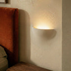 Close-up of the Clérachic trimless wall light's warm glow beside a rust velvet bed headboard.