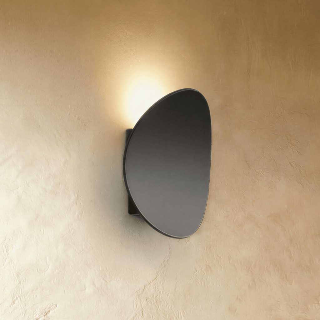 Clérachic's black organic-curve wall light casts a warm upward glow across a textured plaster wall.