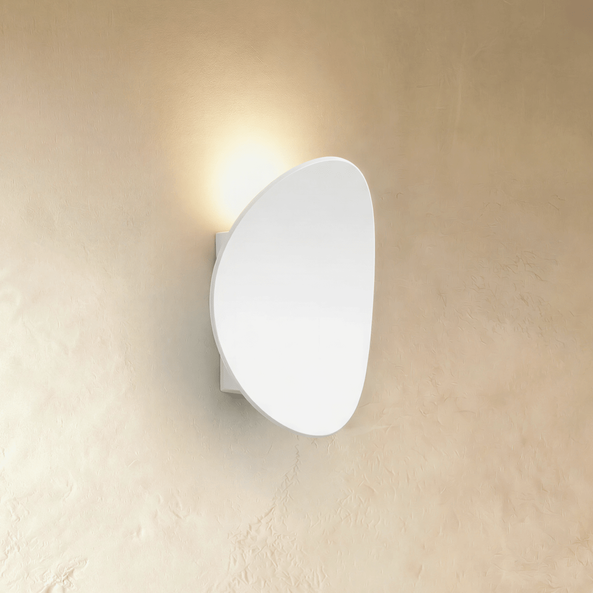 Clérachic's white pebble-shaped wall light throws soft warm light up a plaster wall in profile view.