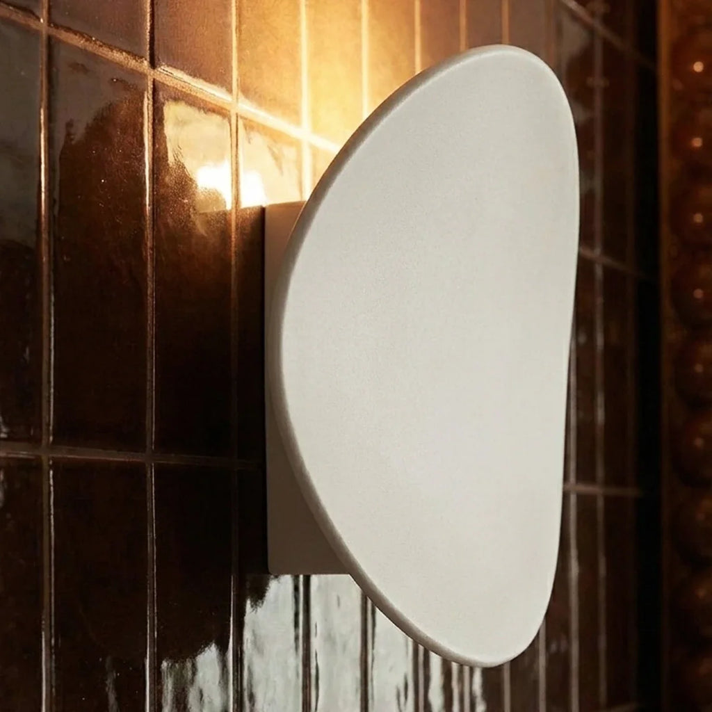Close-up of a Clérachic white wall light glowing softly beside dark glossy bathroom tile and a bronze mirror frame.