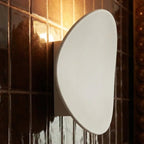 Close-up of a Clérachic white wall light glowing softly beside dark glossy bathroom tile and a bronze mirror frame.