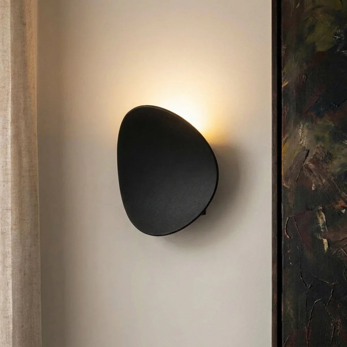 Close-up of a Clérachic black wall light glowing warm in a hallway corner beside a textured painting edge.