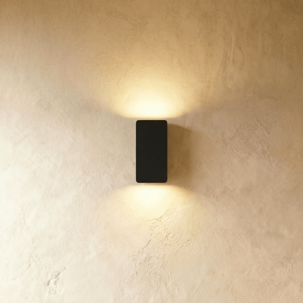 Clérachic black aluminium wall light casts warm up-and-down glow on a plaster wall, smallest rectangular size.