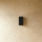 Clérachic black aluminium wall light shown unlit, its compact rectangular body mounted flush to a plaster wall.
