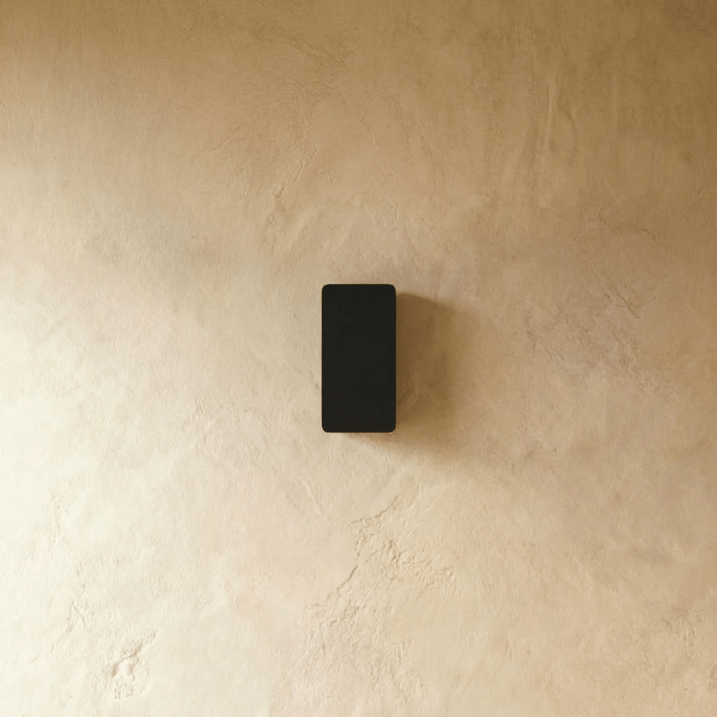 Clérachic black aluminium wall light shown unlit, its compact rectangular body mounted flush to a plaster wall.