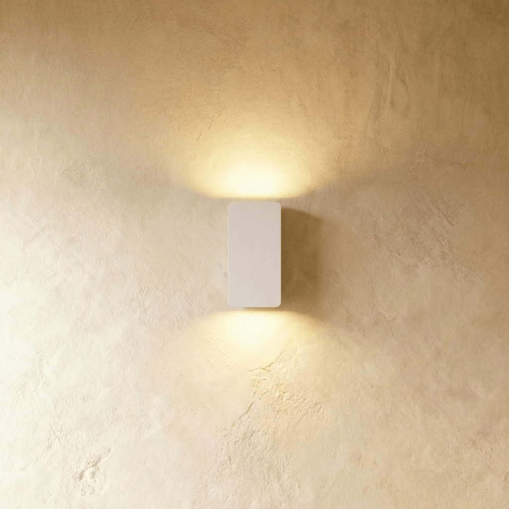 Clérachic white aluminium wall light, compact rectangular body, casts warm up-and-down glow on a plaster wall.