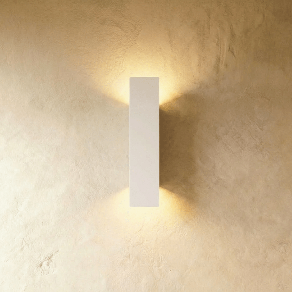 Clérachic white aluminium wall light in a medium bar profile, warm light washing up and down a plaster wall.