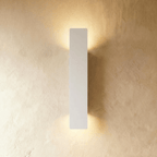 Clérachic white aluminium wall light, taller bar profile, casts warm light up and down a textured plaster wall.