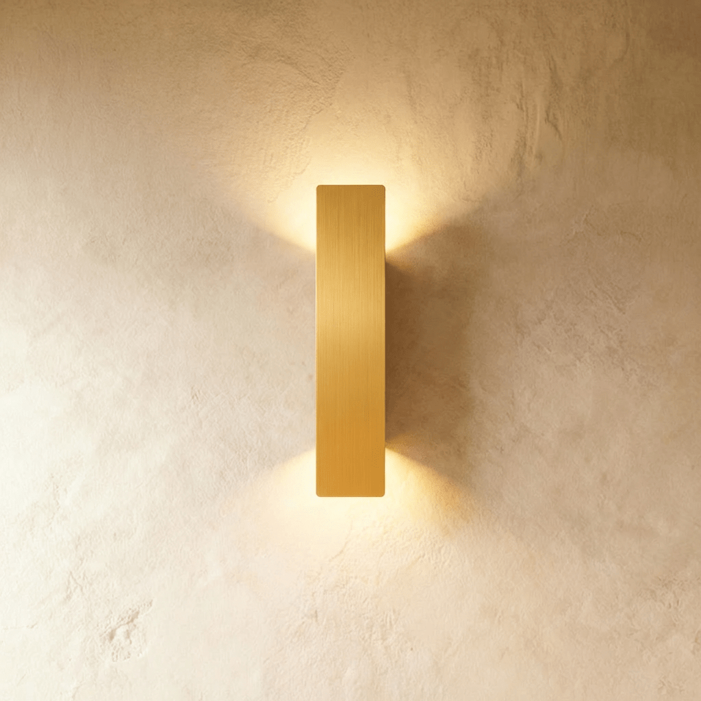 Clérachic brushed gold aluminium wall light casts warm up-and-down light on a textured plaster wall.
