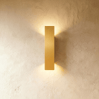 Clérachic brushed gold aluminium wall light casts warm up-and-down light on a textured plaster wall.