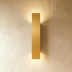 Clérachic brushed gold aluminium wall light in a longer bar profile, light washing a plaster wall top and bottom.