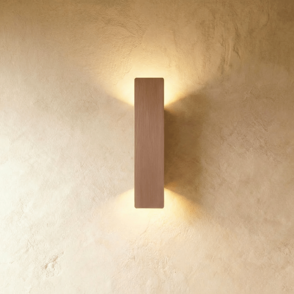Clérachic coffee-toned aluminium wall light casts warm up-and-down light on a textured plaster wall.