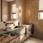 Clérachic white wall light glows warm on a zellige-tiled bathroom wall beside a green marble vanity counter.
