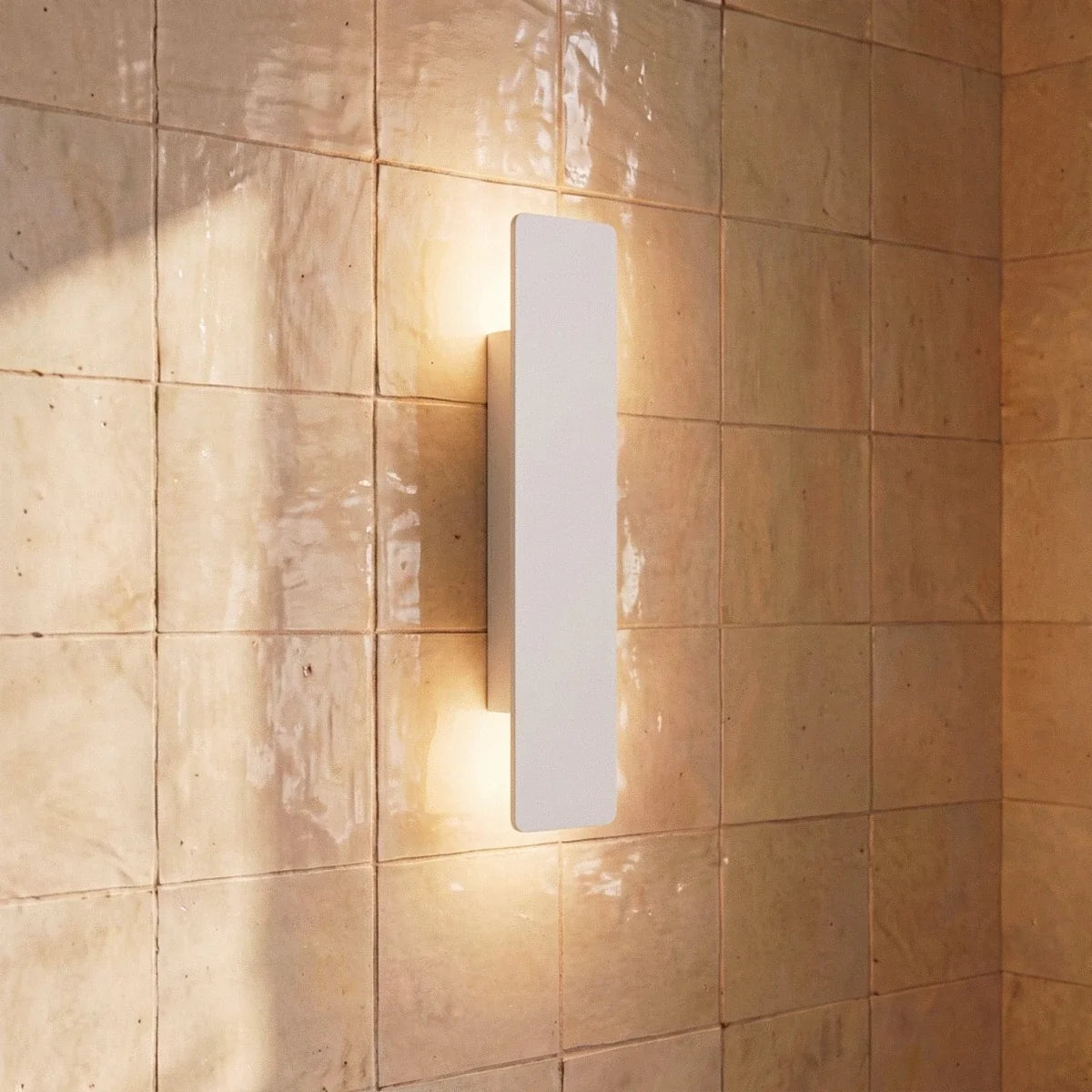 Clérachic white wall light close-up shows warm up-and-down light against a glossy beige zellige tile wall.