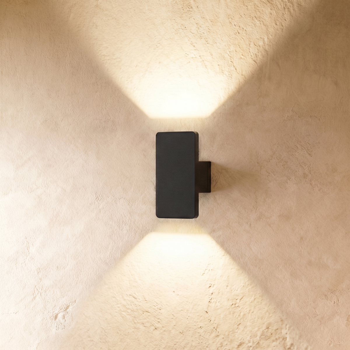 A compact Clérachic black wall light casts up-and-down light beams across a warm plastered wall in an X pattern.