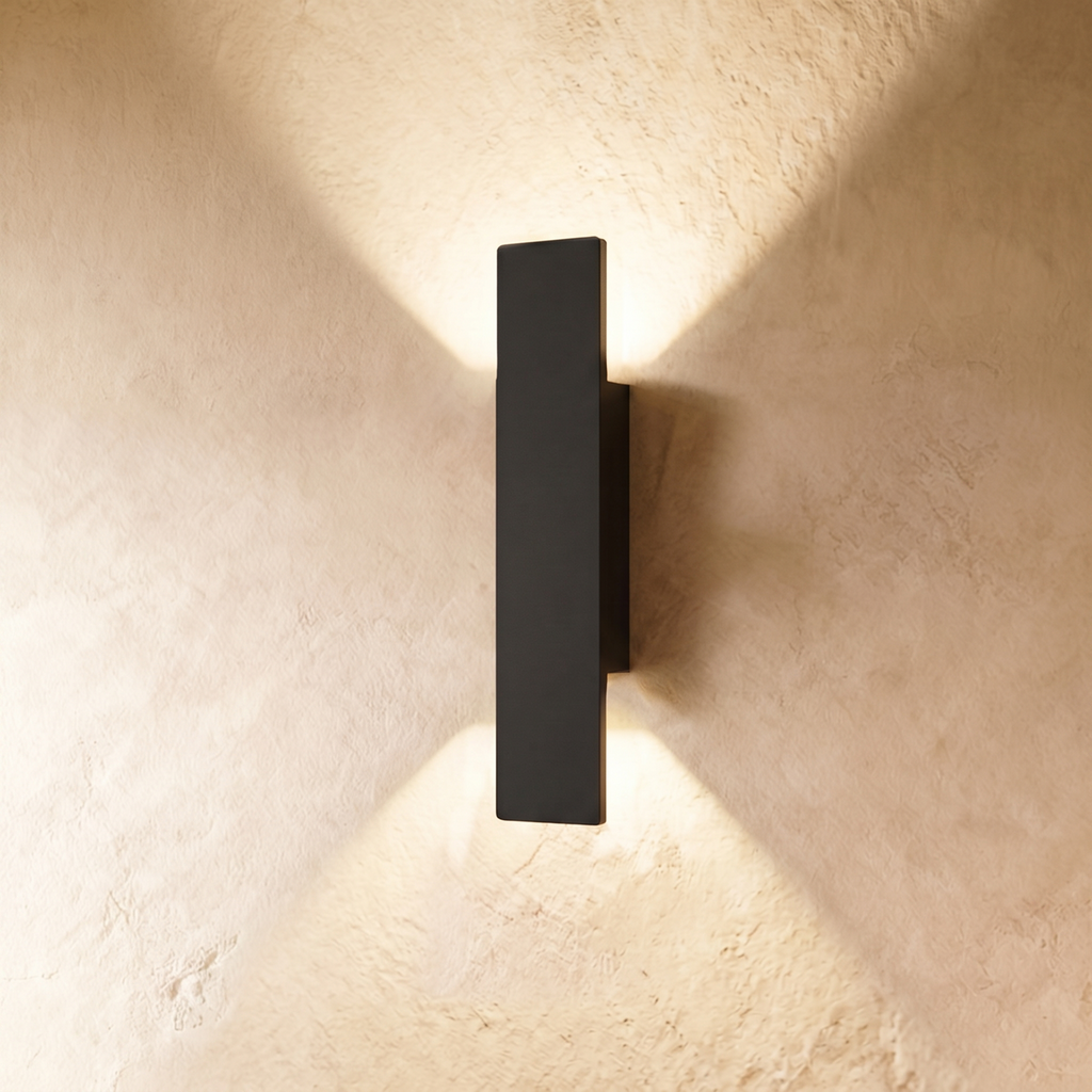 A taller Clérachic black wall light throws warm up-and-down beams across a textured plastered wall surface.