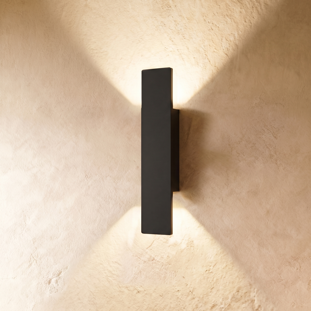 A taller Clérachic black wall light throws warm up-and-down beams across a textured plastered wall surface.