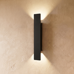 This longer Clérachic black wall light spans a wide plastered panel, warm light spreading above and below it.