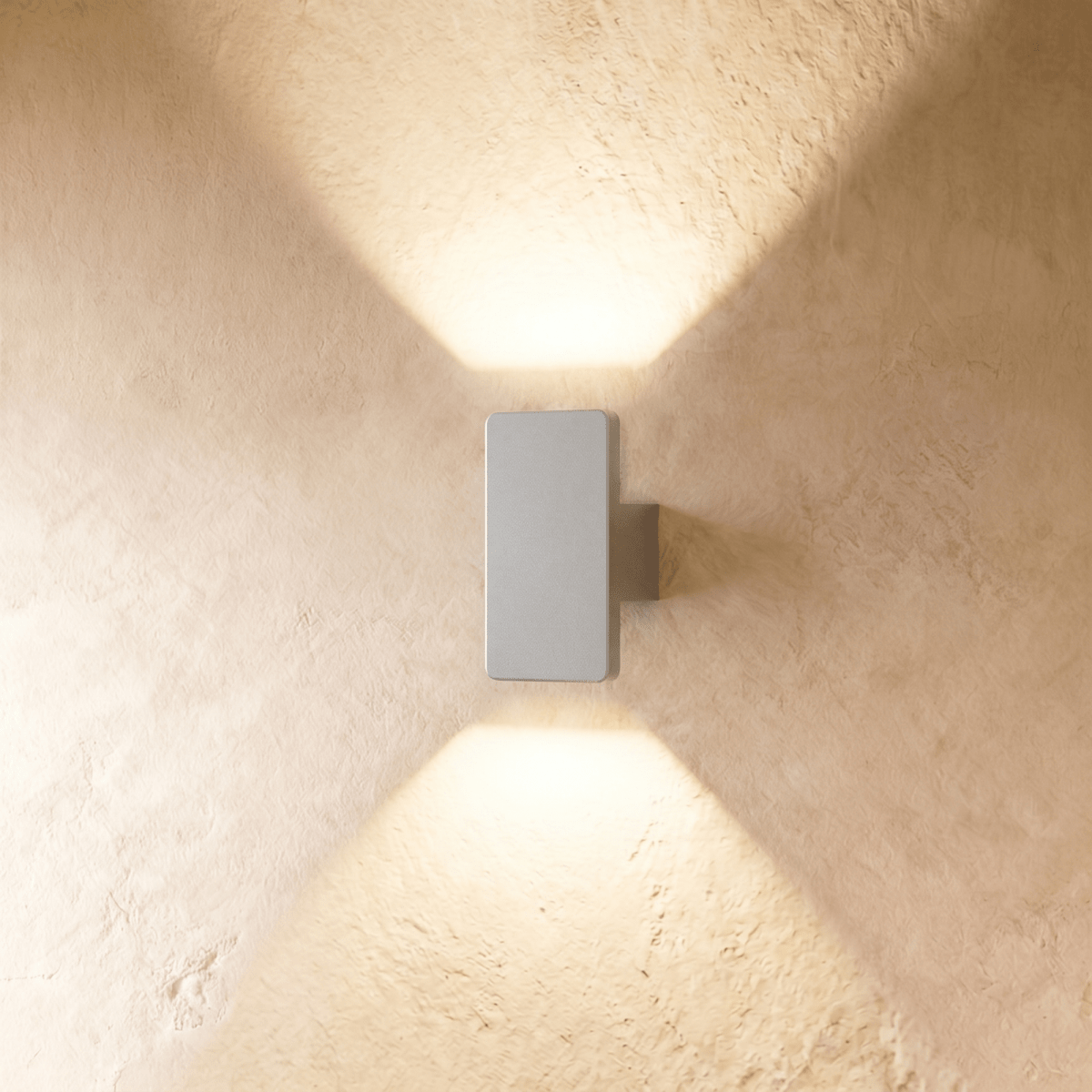 A compact Clérachic white wall light casts warm up-and-down beams across a sunlit plastered wall surface.