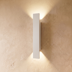 This longer Clérachic white wall light spans a wide plastered panel, warm light spreading above and below it.