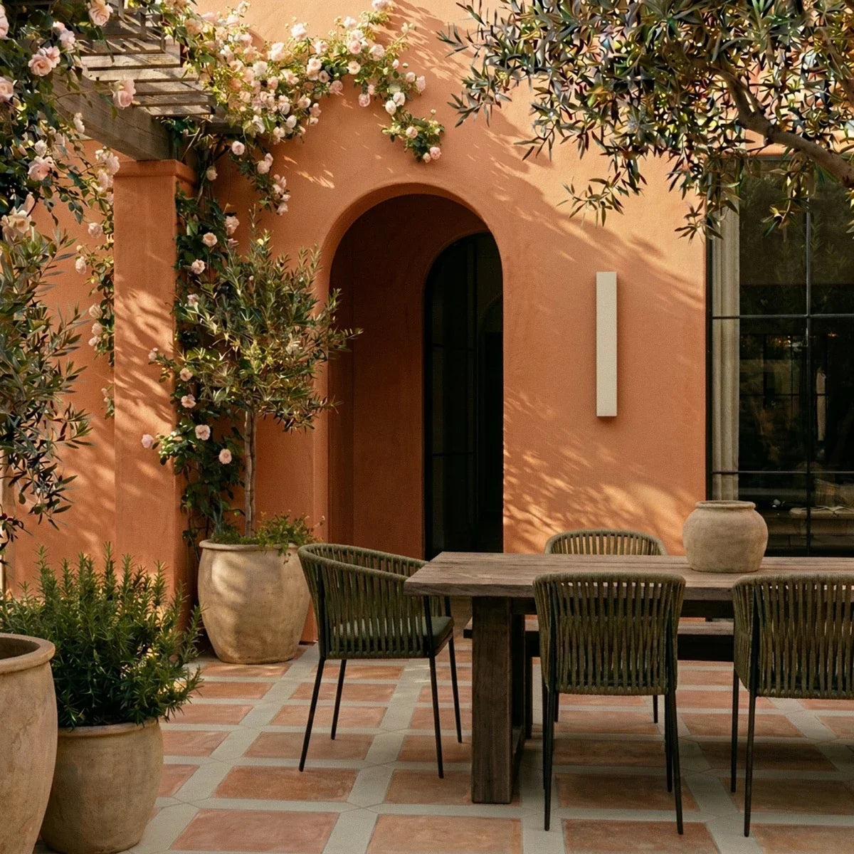 A Clérachic white wall light sits beside an arched doorway on a terracotta courtyard wall set for outdoor dining.