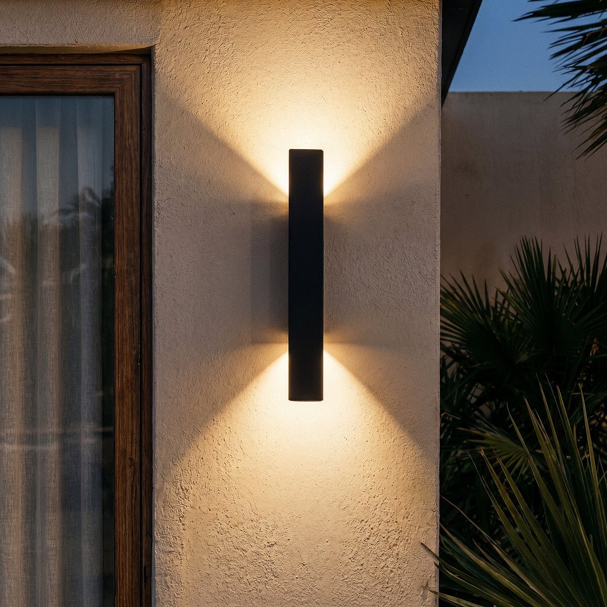 Close night view of the Clérachic black wall light shows its beams fanning across a stucco pillar corner.