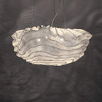 The ruffled white shade of this Clérachic pendant glowing against a dark grey wall marked with soft shadow patterns.