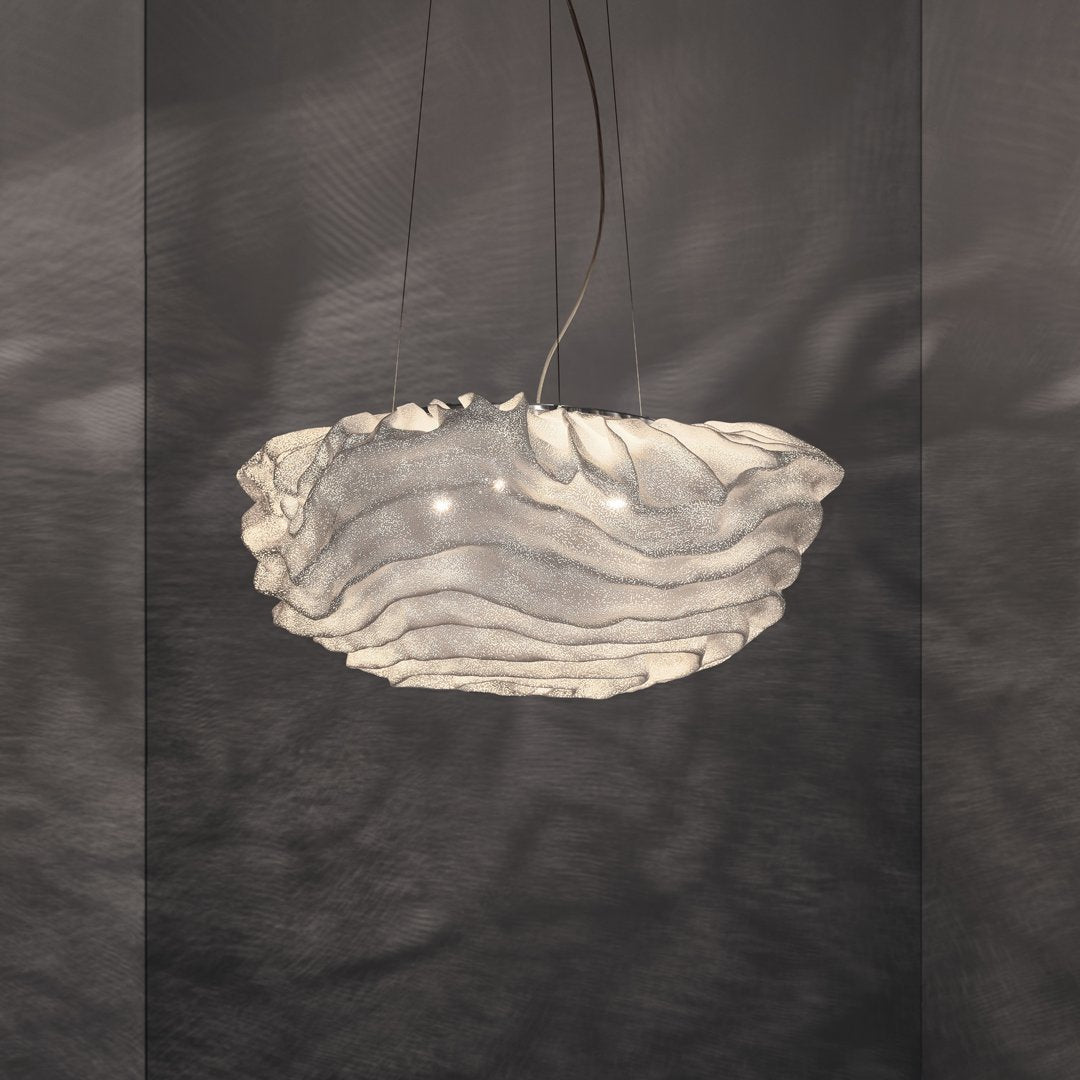A smaller view of this Clérachic pendant lit against a dark grey wall, its layered mesh edges catching the light.