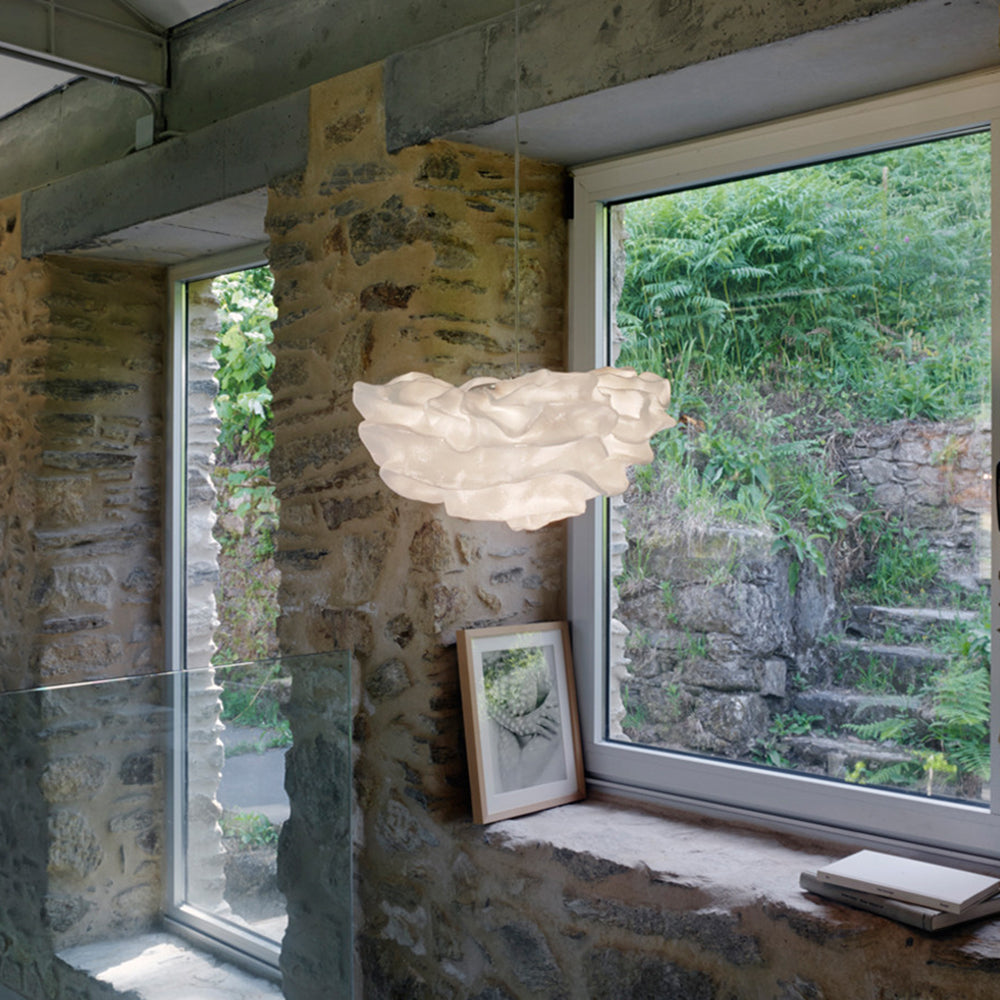 In a stone-walled room beside a sunny window, a Clérachic pendant with a cloud-like white shade hangs above a framed print.