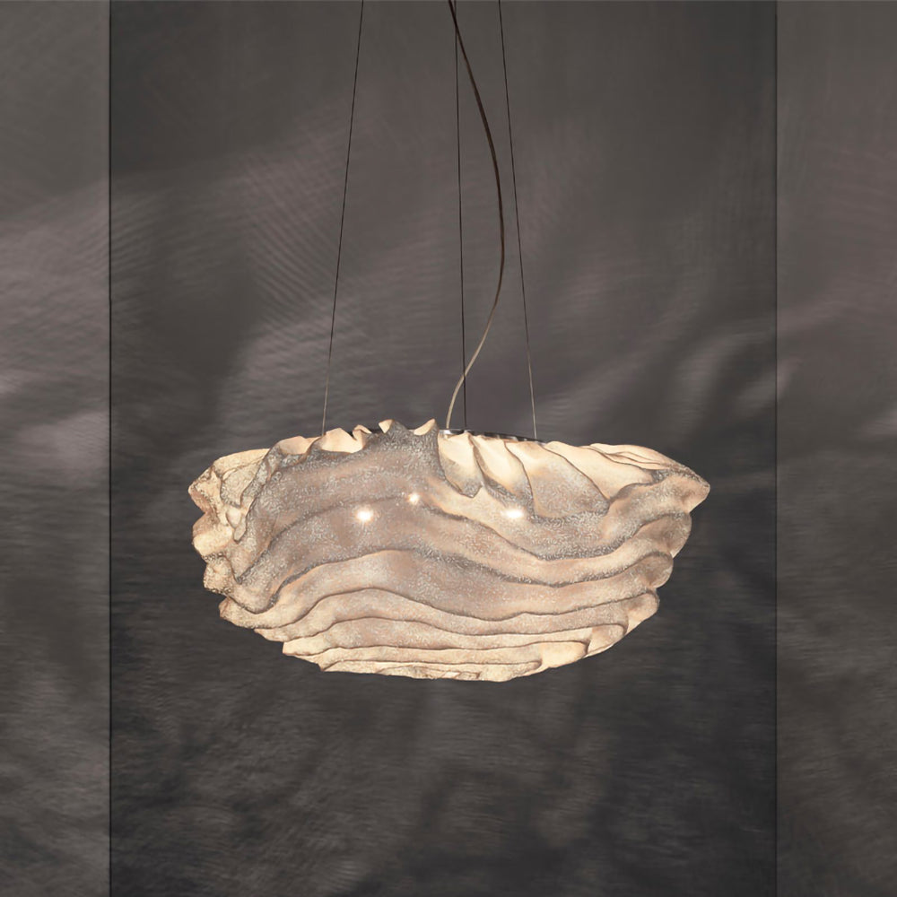 Warm light glows through the layered shade of this Clérachic pendant, set against a dark grey wall with soft ripples of shadow.